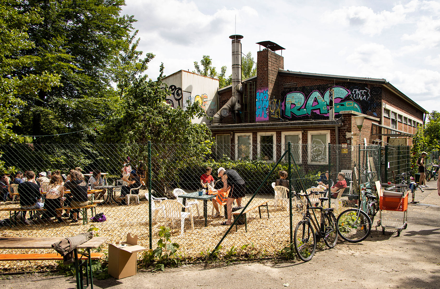 Cafebetrieb vorm Pumpenhaus, Menschen sitzen an Tischen und Stühlen und die Sonne scheint